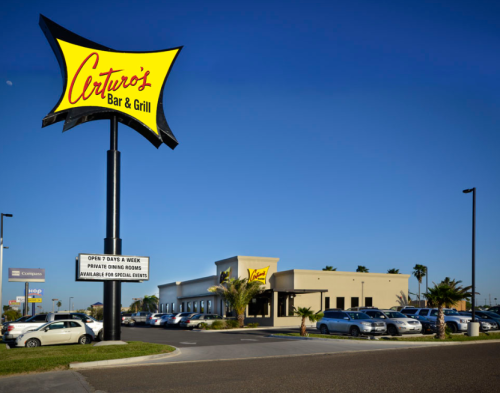 Sign for Ceturio's Bar & Grill with a clear blue sky and parking lot filled with cars.