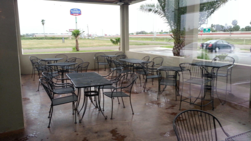 Empty outdoor seating area with metal tables and chairs, overlooking a highway and palm trees in the background.