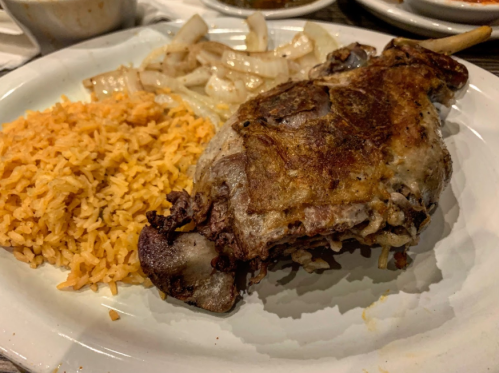 A plate featuring a crispy chicken leg, seasoned rice, and sautéed onions.