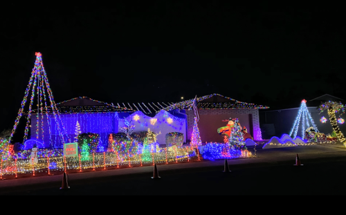 A brightly lit house decorated with colorful Christmas lights, featuring trees and festive displays at night.