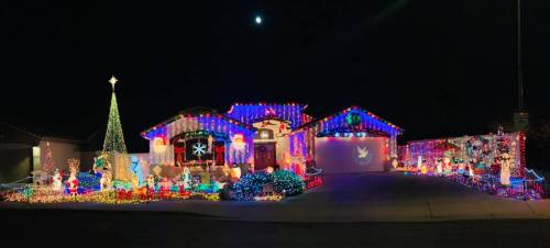 A brightly lit house decorated with colorful Christmas lights, featuring a large tree and festive displays.