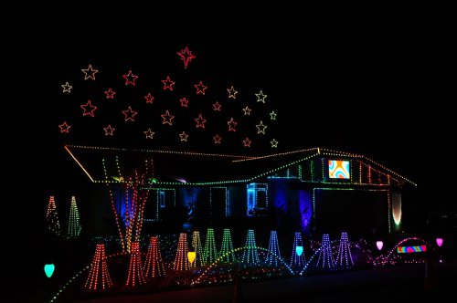 A house decorated with colorful Christmas lights, featuring star shapes and vibrant patterns against a dark night sky.