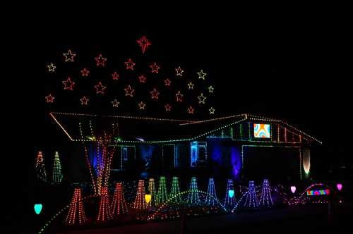 A house decorated with colorful Christmas lights, featuring star shapes and vibrant patterns against a dark night sky.