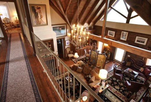 A spacious, rustic living room with high ceilings, wooden beams, and elegant furnishings, viewed from a balcony.