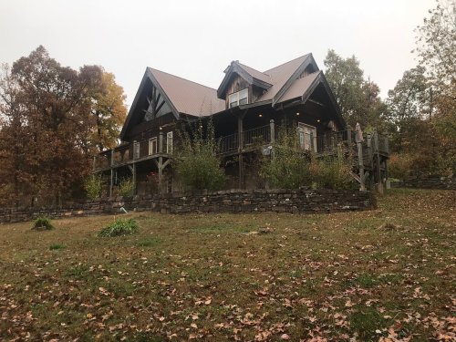 A rustic wooden house with a sloped roof, surrounded by autumn foliage and a stone wall.