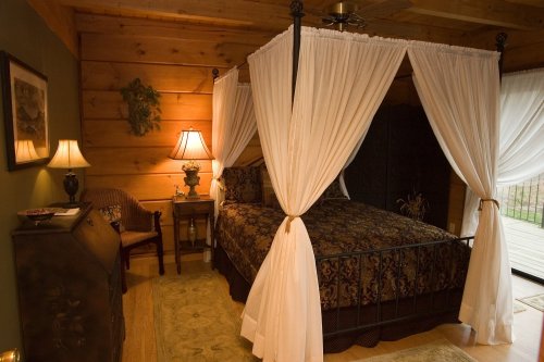 Cozy bedroom with a four-poster bed, draped curtains, wooden walls, and warm lighting from bedside lamps.
