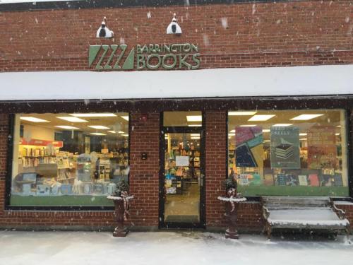 A cozy bookstore, Barrington Books, with snow falling outside and books displayed in large windows.