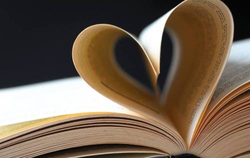 A close-up of an open book with pages forming a heart shape against a dark background.