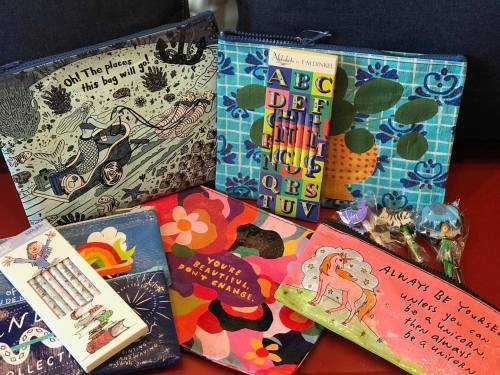 A collection of colorful bags and notebooks with inspirational quotes and designs, arranged on a table.