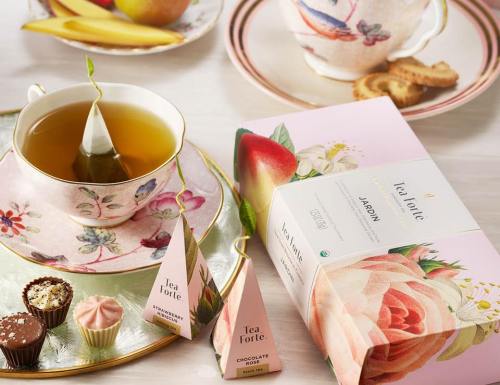 A beautifully arranged tea setting with a cup of tea, pastries, and a box of Tea Forte tea pyramid infusers.