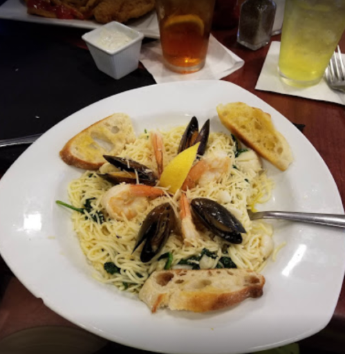 A plate of pasta with shrimp, mussels, and lemon, garnished with toasted bread, served on a wooden table.