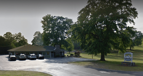A building with a stone facade and several parked cars, surrounded by trees and a sign for a nearby location.