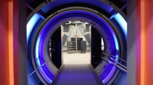 A futuristic tunnel with blue lighting, leading to a spiral staircase in a modern interior space.