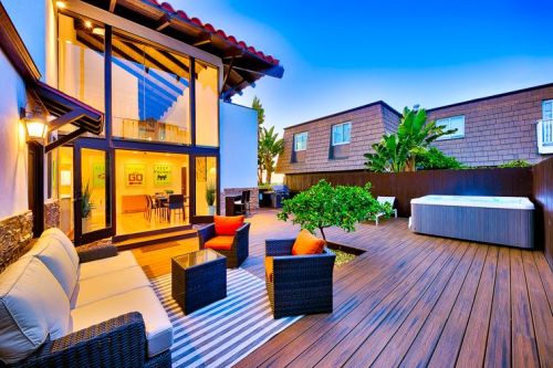 A modern outdoor patio with seating, a hot tub, and lush greenery, set against a twilight sky.