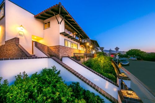 A modern house with a tiled roof, surrounded by greenery, at dusk with soft lighting and a clear blue sky.