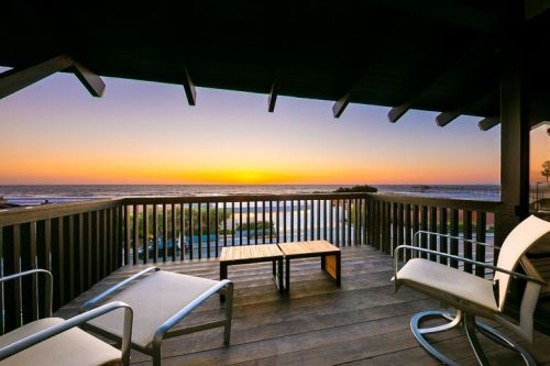 A serene balcony view overlooking the ocean at sunset, featuring two chairs and a small table.