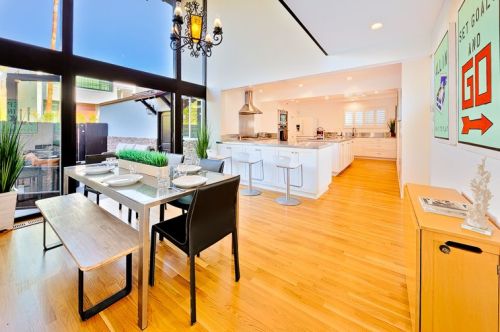 Bright, modern dining area with a wooden table, black chairs, and an open kitchen featuring white cabinetry and stainless appliances.