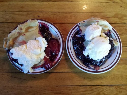 Two plates of dessert featuring fruit compote topped with ice cream and whipped cream, served on wooden table.