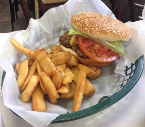 A sesame seed bun burger with lettuce, tomato, and a side of golden French fries in a green basket.