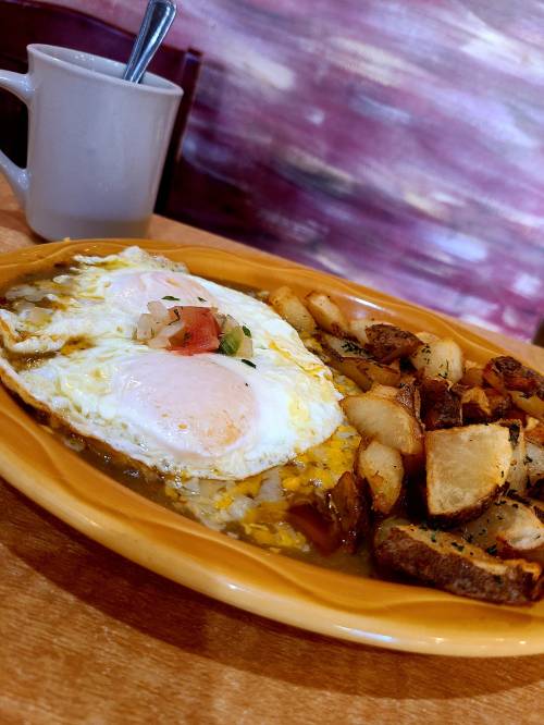 A plate of eggs with a side of seasoned potatoes, served with a cup of coffee in the background.
