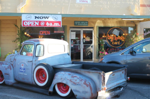 A vintage truck parked outside a café with a welcoming sign and "Open at 6 a.m." displayed.