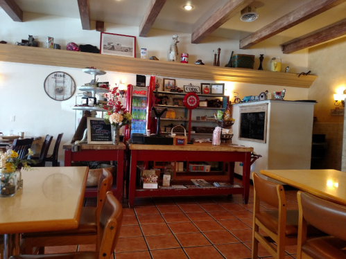 Cozy café interior with wooden beams, a counter displaying drinks, and shelves filled with decor and snacks.