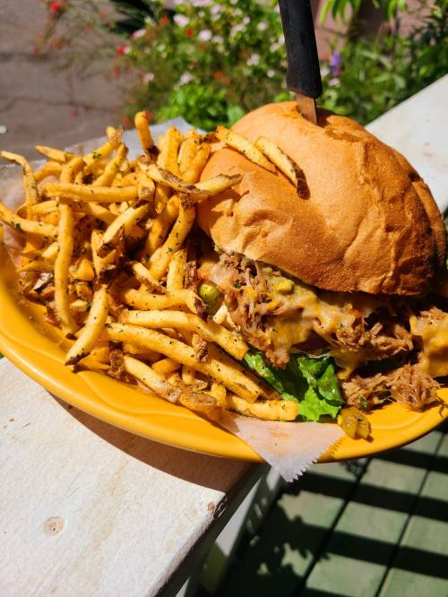 A hearty sandwich with pulled pork, cheese, and lettuce, served with a side of crispy fries on a yellow plate.