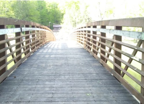 A wooden bridge with a curved design, leading into a bright, green landscape.