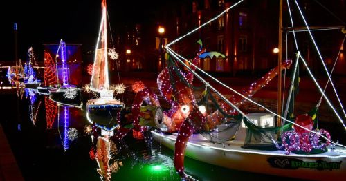 Colorful boats decorated with lights and an octopus display reflect on the water at night.