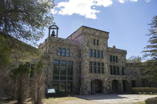 Historic stone building with large windows and a bell tower, surrounded by trees under a clear blue sky.