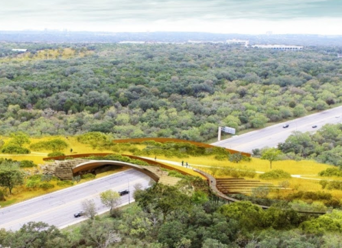 Aerial view of a landscaped bridge over a highway, surrounded by lush greenery and trees.