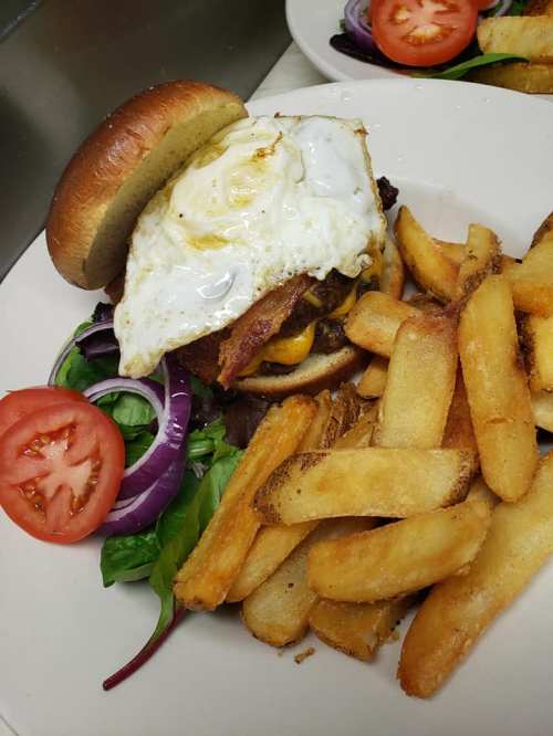 A juicy burger topped with a fried egg, bacon, and cheese, served with fries and fresh vegetables on the side.