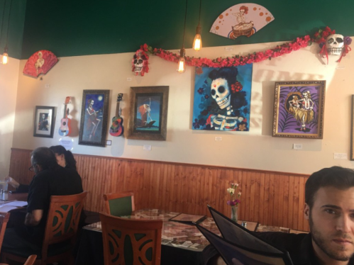 A vibrant restaurant interior featuring colorful artwork, including skeletons and guitars, with patrons seated at tables.