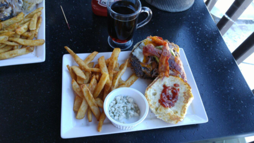 A plate with a burger topped with bacon and cheese, served with fries and a side of blue cheese dressing and ketchup.
