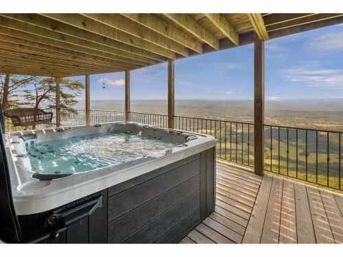 A hot tub on a wooden deck with a scenic view of rolling hills and a clear sky in the background.