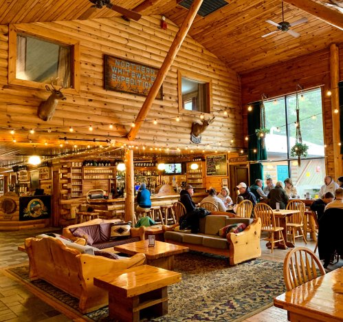 Cozy wooden interior of a lodge with rustic decor, seating areas, and patrons enjoying food and drinks.