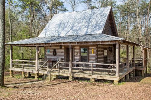 A rustic wooden cabin with a metal roof, surrounded by trees and featuring a spacious porch with railings.