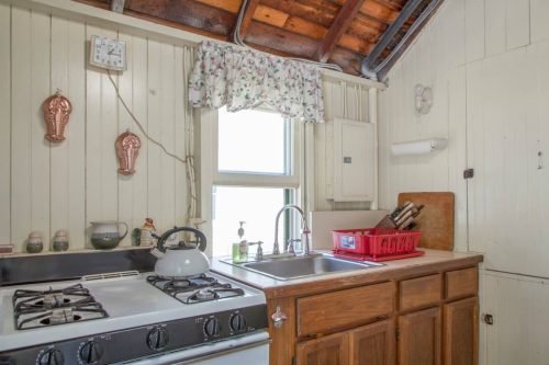 A cozy kitchen with a gas stove, sink, wooden cabinets, and a window adorned with floral curtains.