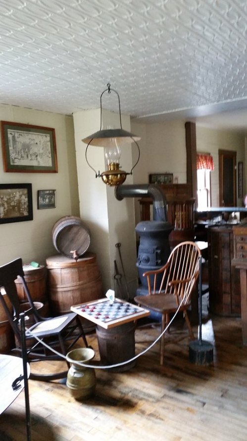 A cozy vintage room with a wooden floor, a lantern, a stove, and rustic furniture, including a checkered table.
