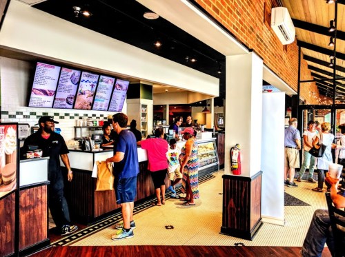 A busy restaurant interior with customers ordering at the counter and a line of people waiting. Bright and modern decor.