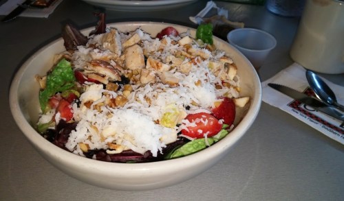 A bowl of salad with mixed greens, strawberries, shredded chicken, nuts, and a sprinkle of shredded coconut on top.