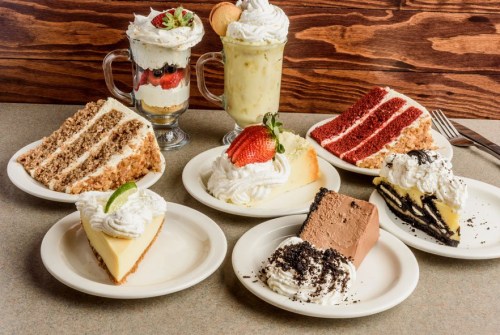 A variety of desserts on plates, including cakes, pies, and parfaits, all topped with whipped cream and garnishes.