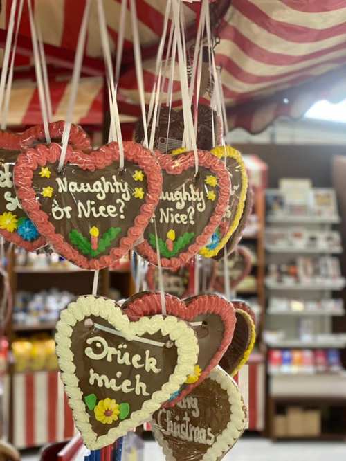 Colorful heart-shaped cookies with messages like "Naughty or Nice?" hanging at a festive market stall.