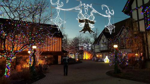 A festive street adorned with colorful lights and decorations, featuring a glowing angel and charming buildings at dusk.