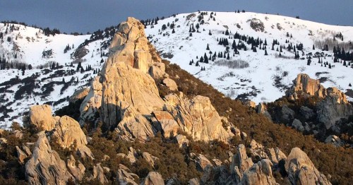 Rocky mountain landscape with snow-capped peaks and rugged terrain under a cloudy sky.