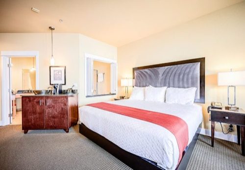 A cozy hotel room featuring a king-sized bed, nightstands, and a small kitchenette area. Bright and inviting decor.