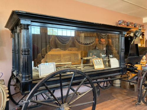 A vintage horse-drawn hearse displayed in a museum, featuring ornate details and historical artifacts.