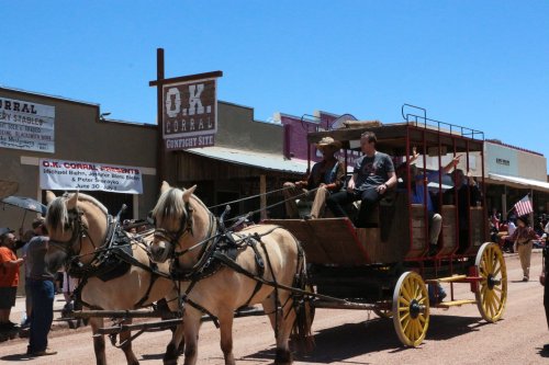 A horse-drawn carriage with passengers rides past the O.K. Corral in a historic western town.