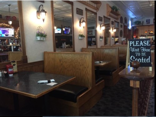 Interior of a restaurant featuring wooden booths, a waiting sign, and decorative wall elements.