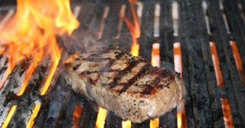 A juicy steak sizzling on a grill, surrounded by flames and grill marks.
